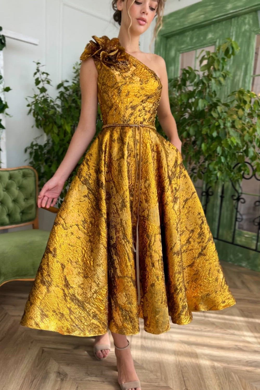 This eye-catching gold dress is made of a beautiful taffeta fabric. It features a structured bodice with boning, a midi-length skirt, and inseam pockets. The dress is adorned with asymmetric handmade floral details, embroidered gold beads, and a unique crafted belt.