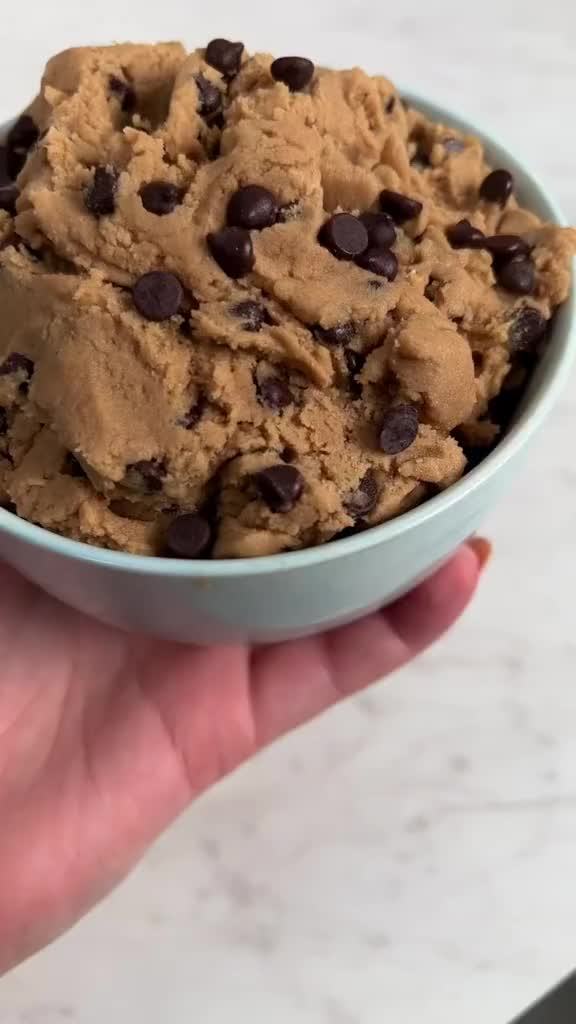 This may contain: a hand holding a bowl filled with chocolate chip cookie ice cream on top of a counter