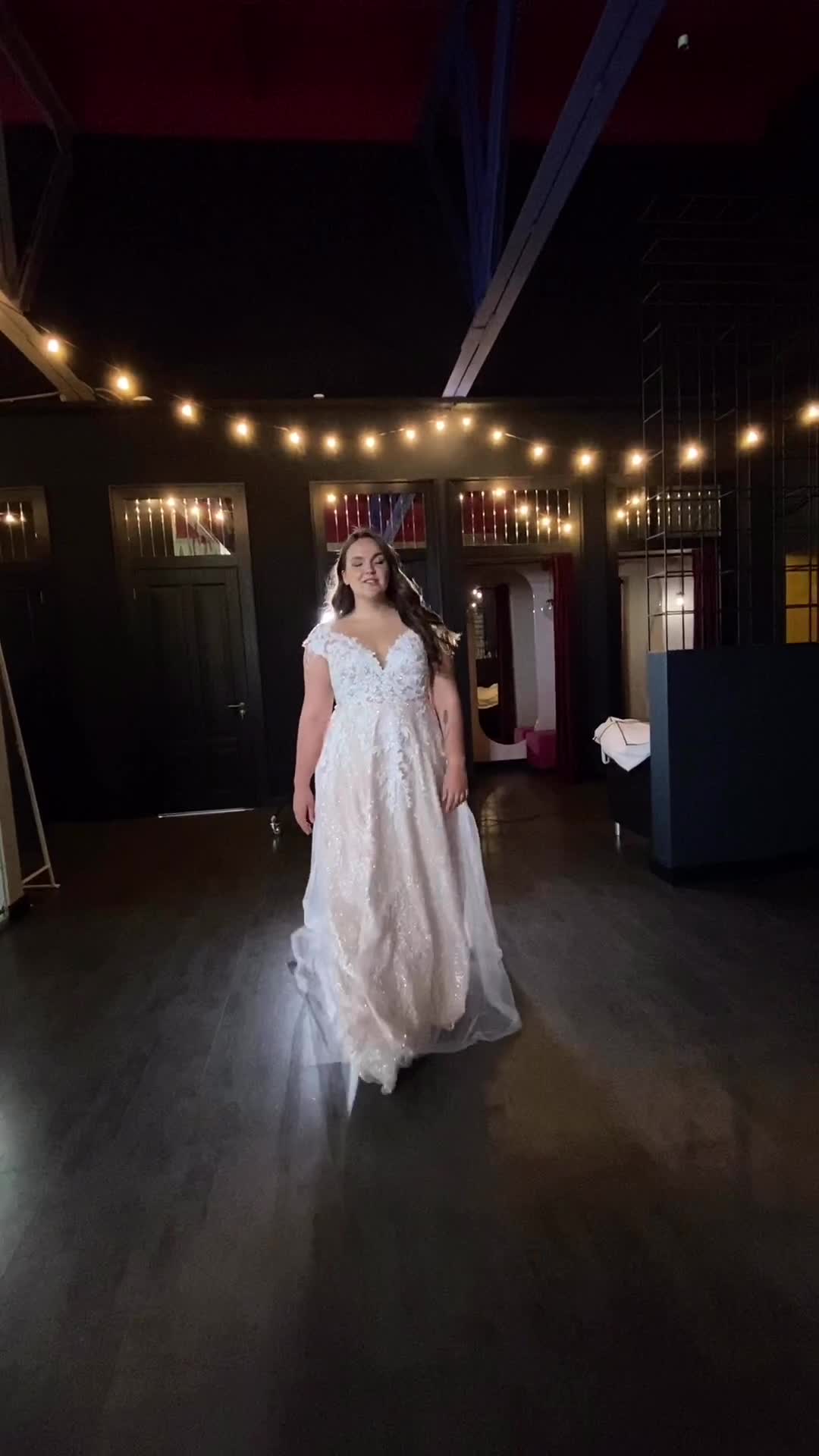 This may contain: a woman in a white dress walking across a dark room with lights on the ceiling