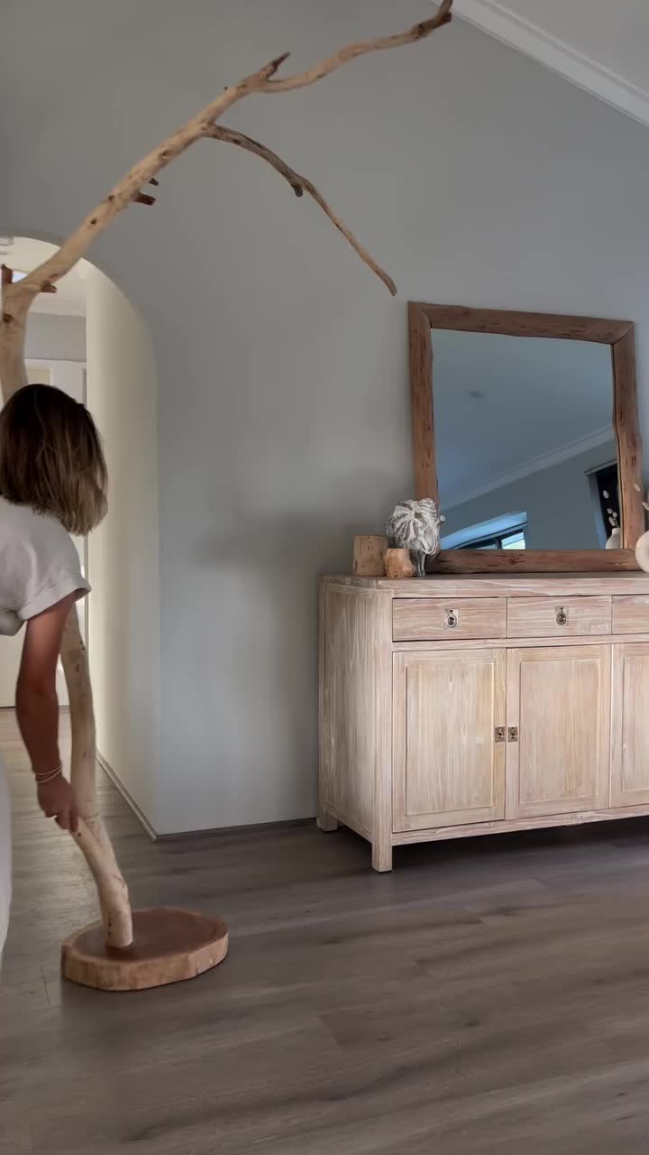 This may contain: a woman bending over to pick something out of a white vase on the floor in front of a mirror