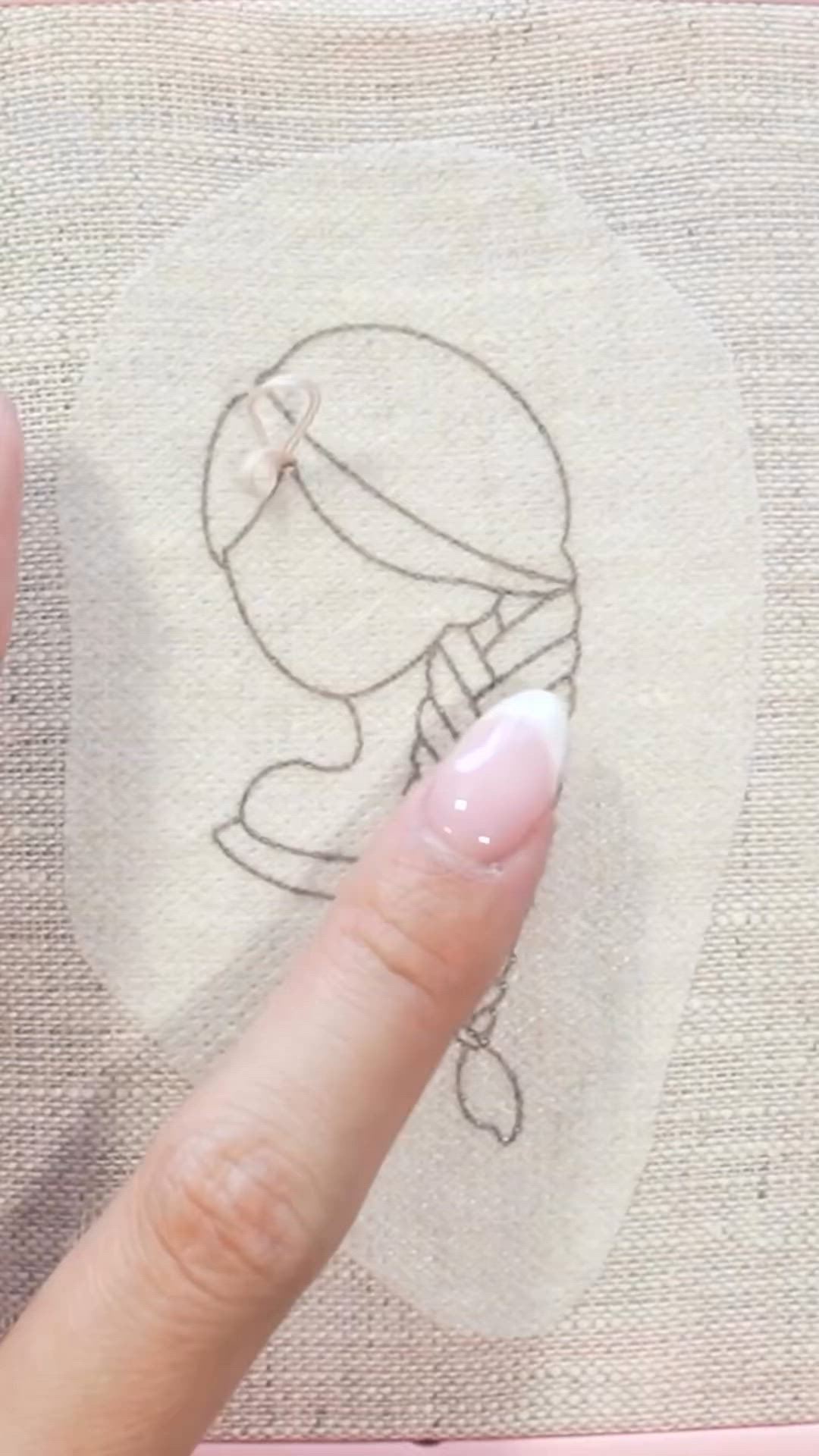 This may contain: a woman's hand with pink nail polish holding up a piece of fabric that has a drawing on it