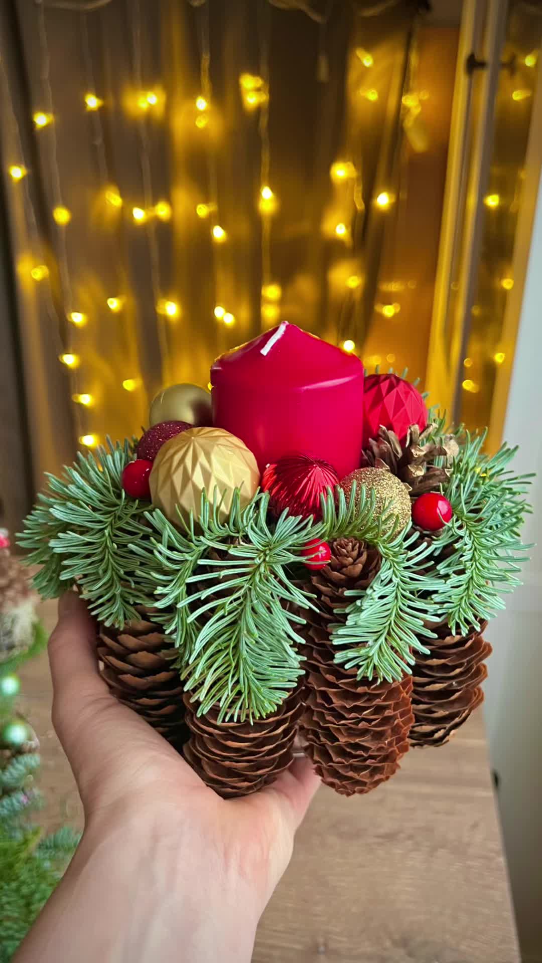 This may contain: a hand holding a pine cone filled with christmas decorations and a red candle in it