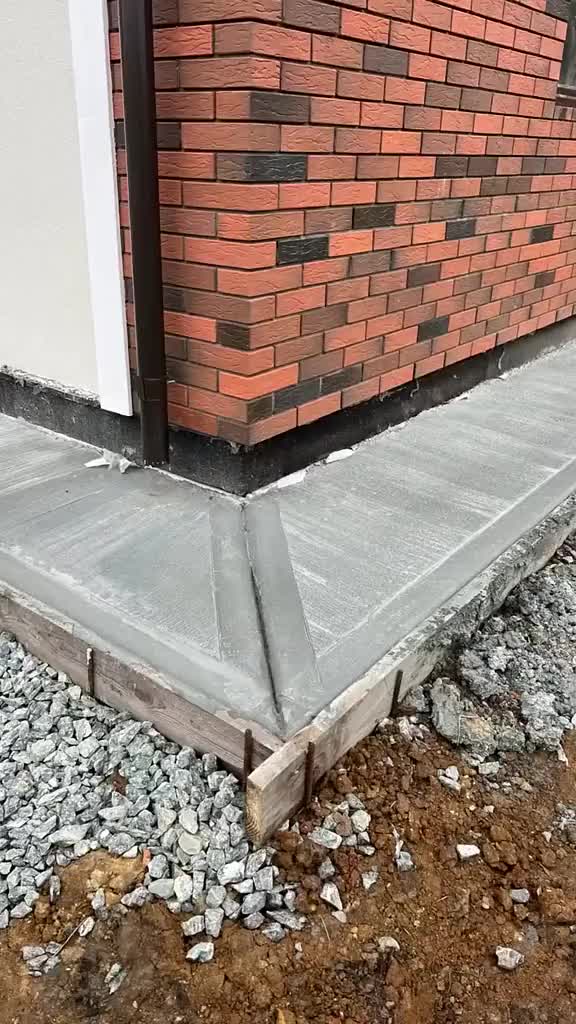 This may contain: the corner of a building with some bricks on it and gravel in front of it