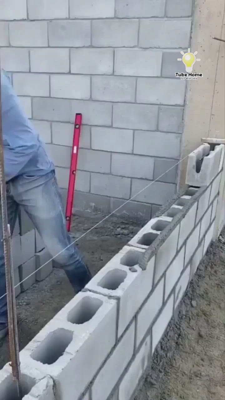 This may contain: a man standing next to a brick wall with cement in his hands and wearing a hat