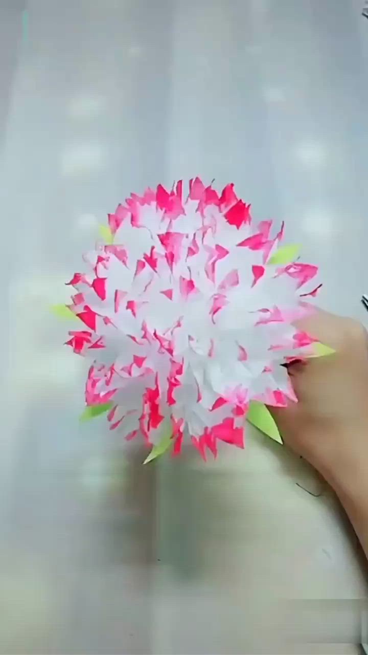 This may contain: a person holding a pink and white paper flower