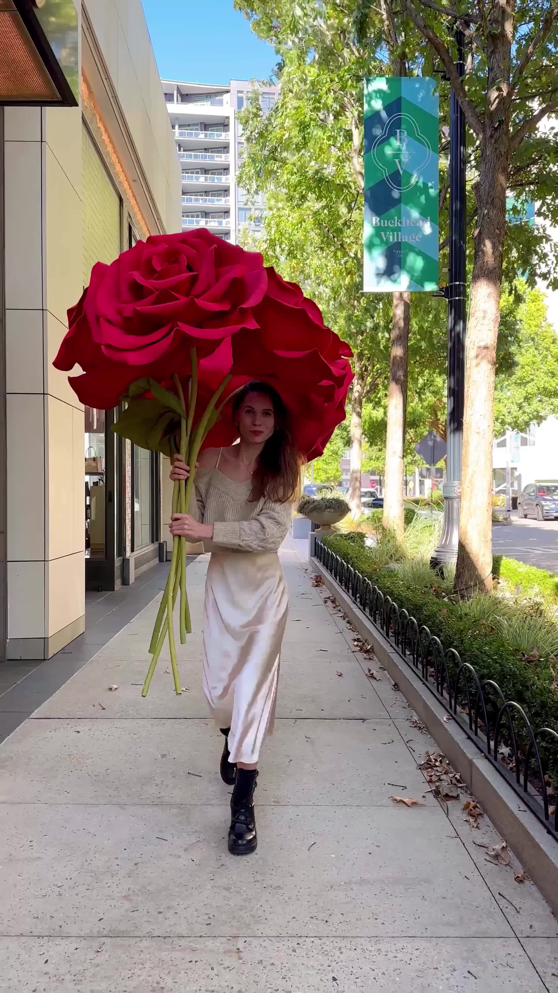 This may contain: a woman is walking down the street with a large red rose in her hand and an umbrella over her head