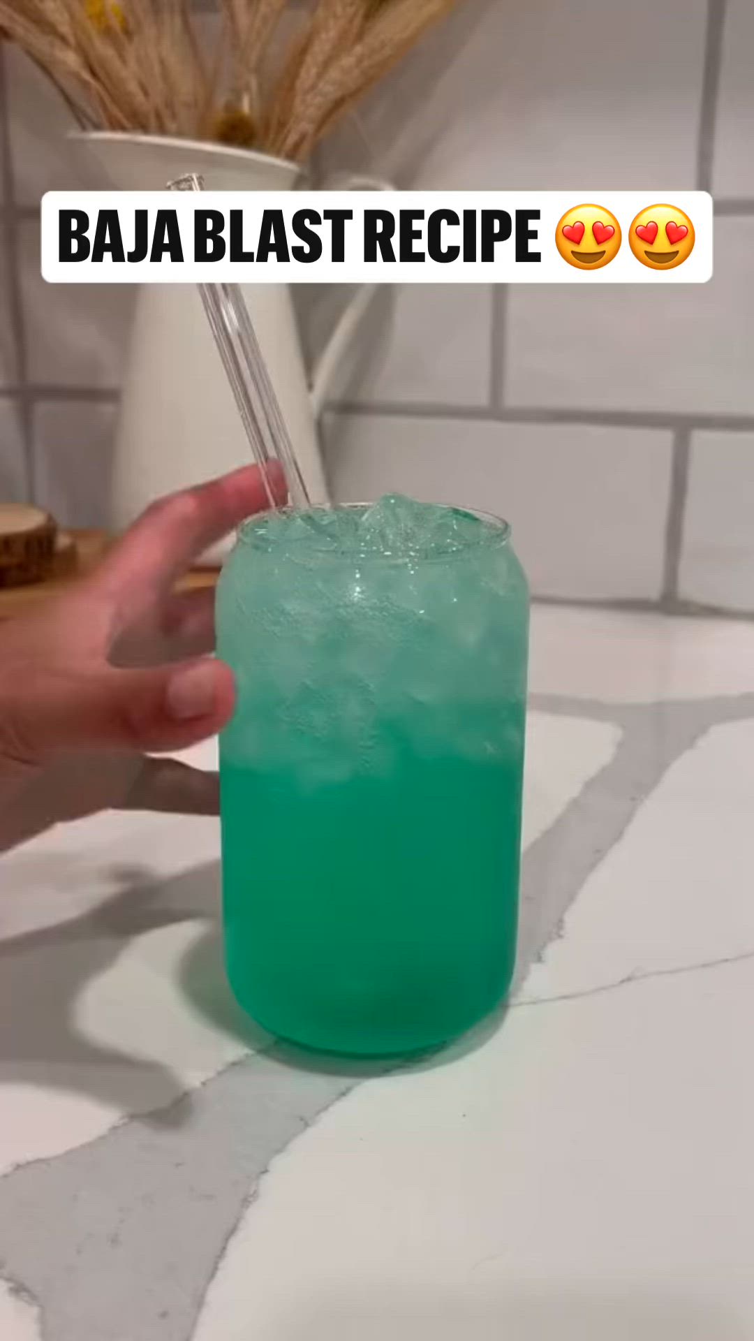 This may contain: a person holding a green drink in front of a white tiled wall with the words baja blast recipe on it