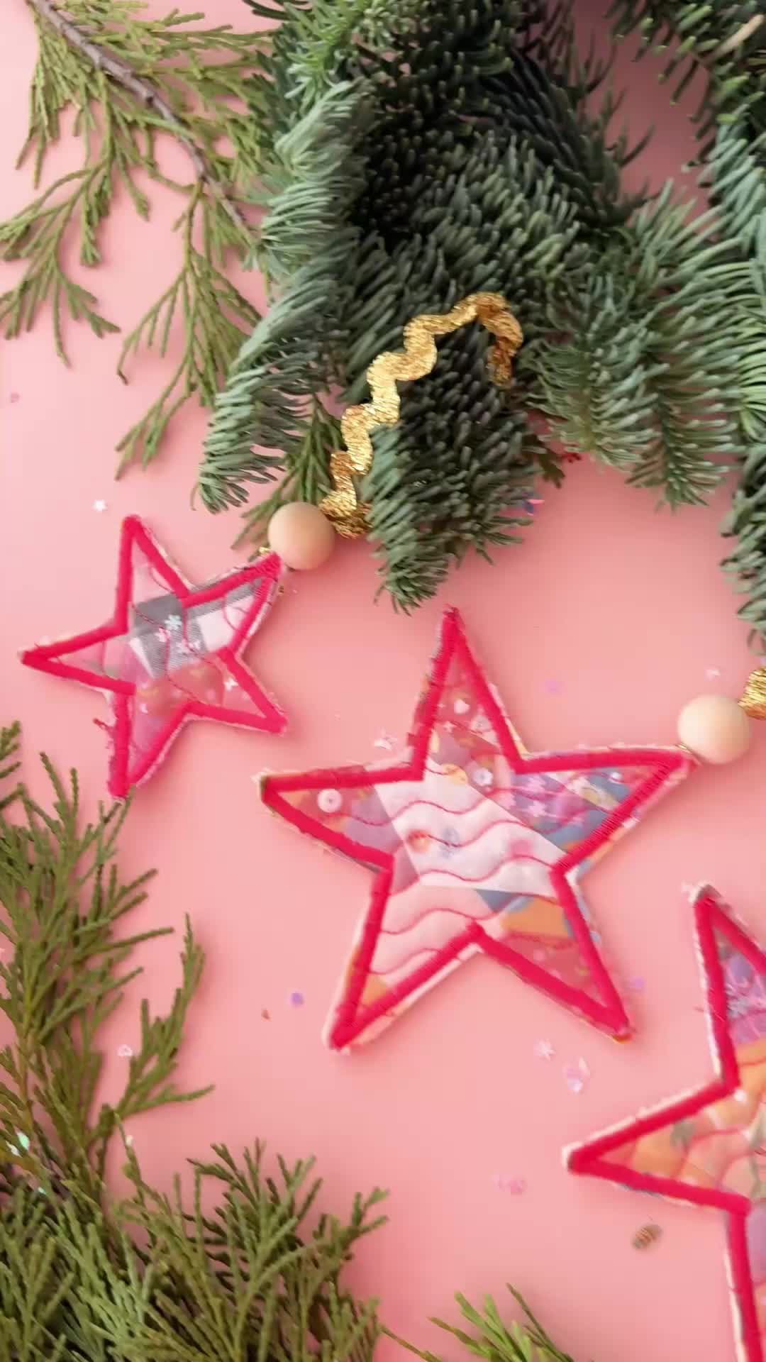 This may contain: three red and white stars are hanging on a pink surface with pine branches in the foreground