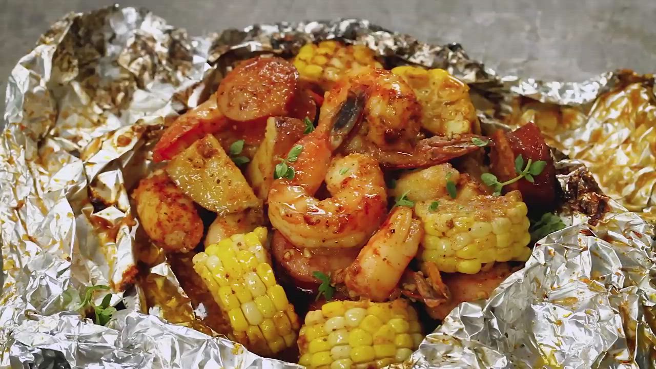 This may contain: shrimp and corn on the cob wrapped in foil