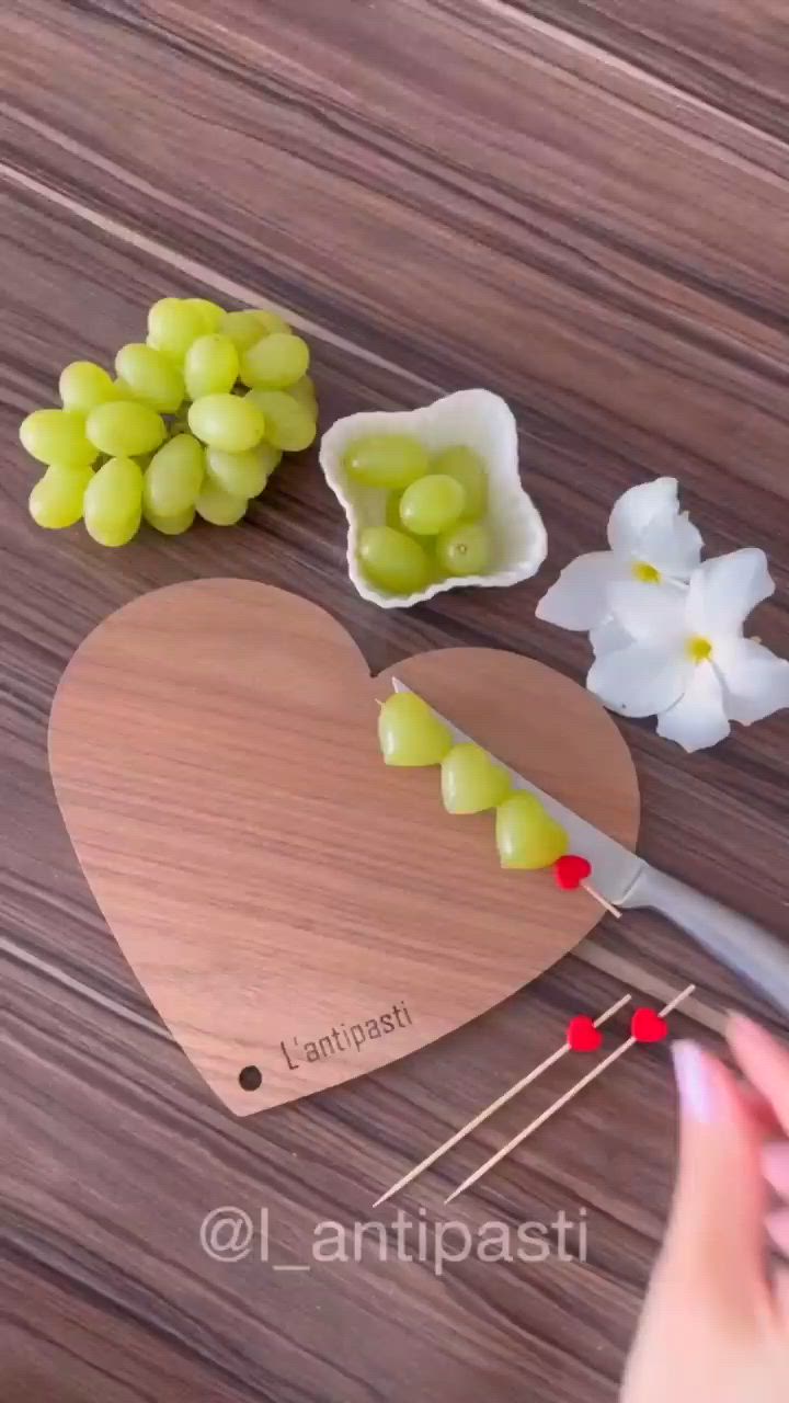 This may contain: there is a heart shaped cutting board with grapes on it and flowers next to it