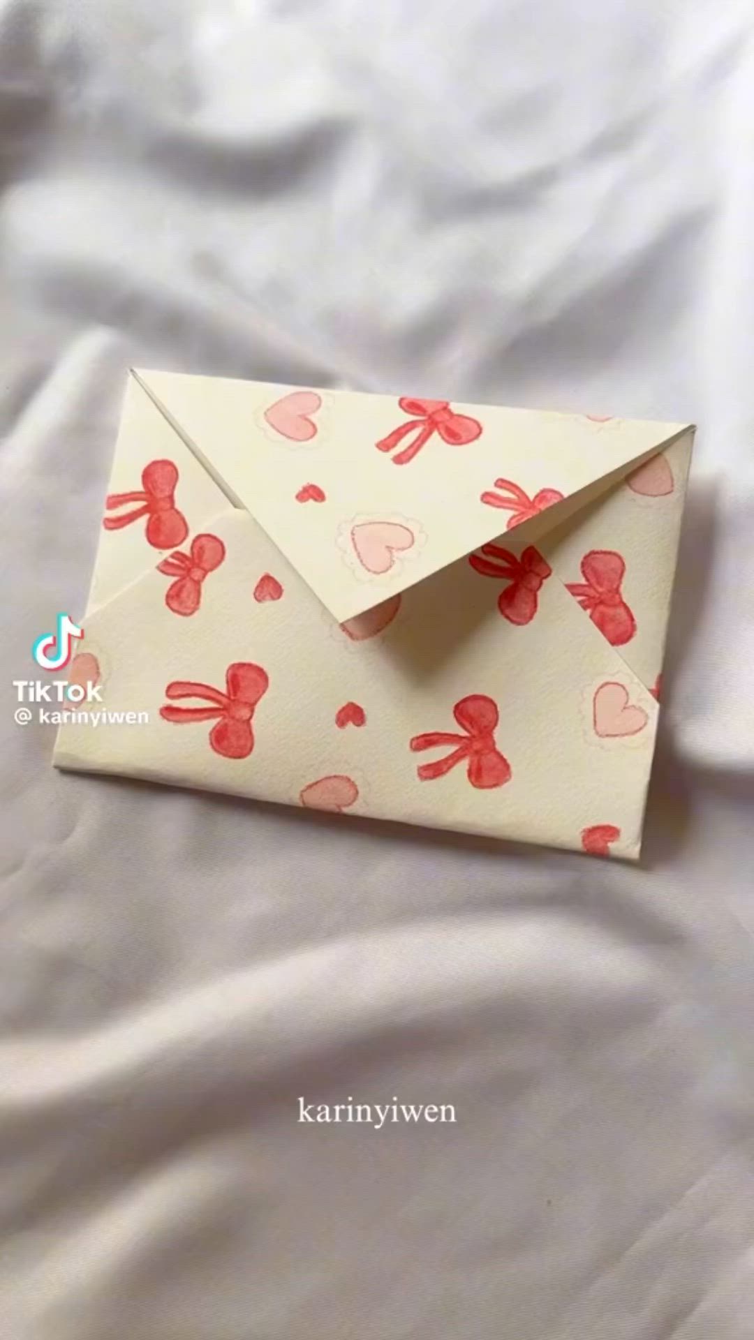 This may contain: an envelope with hearts and bows is on a white sheet covered bed, next to the words hello kitty written in red ink