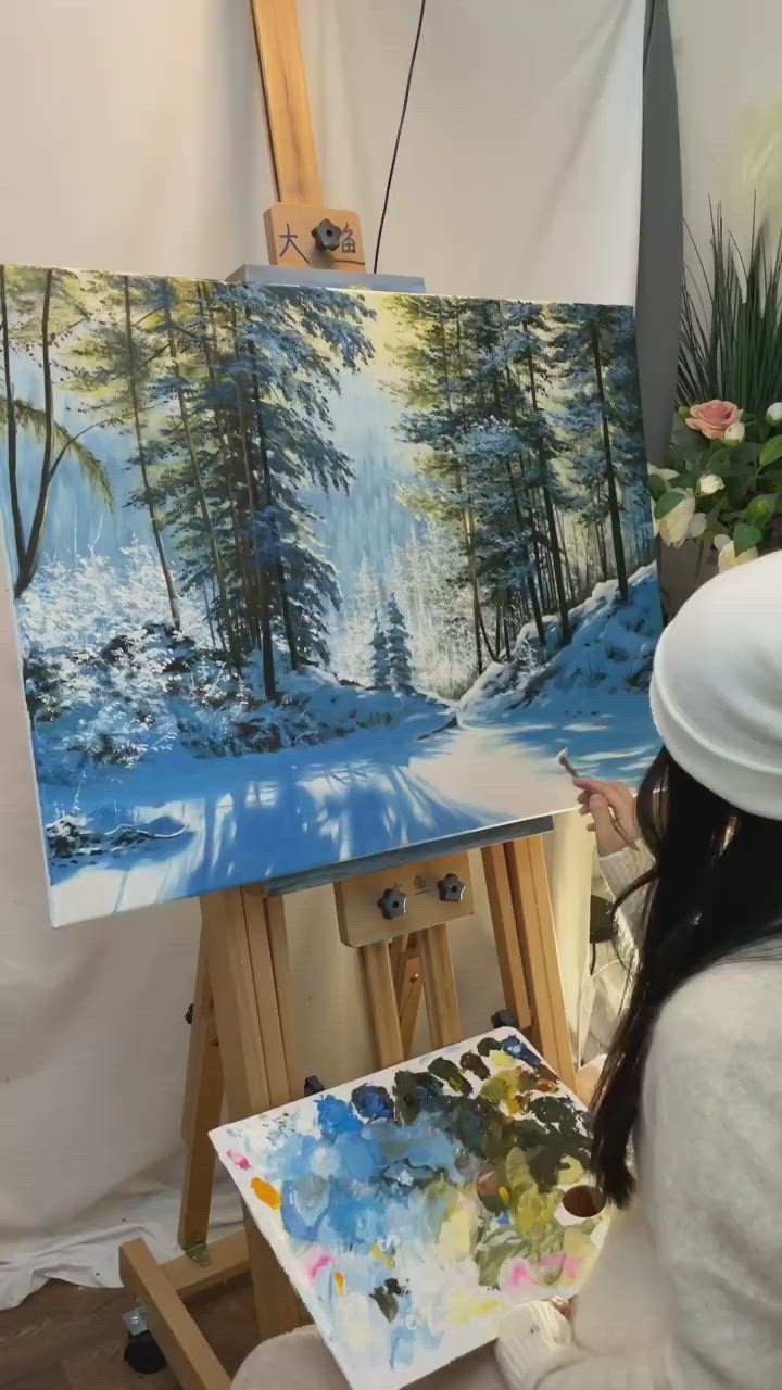 This may contain: a woman is painting on an easel in front of a snowy scene with pine trees