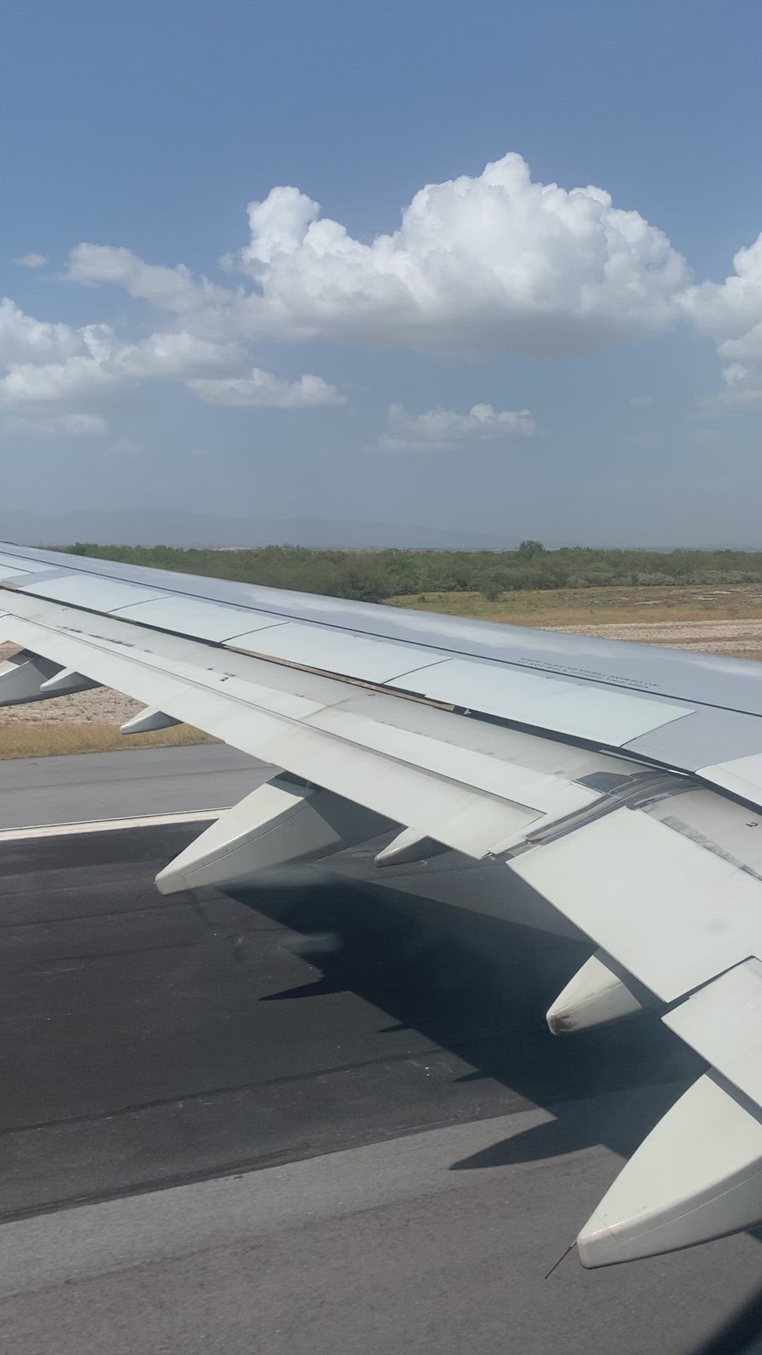 This may contain: the wing of an airplane as it flies over land and clouds in the sky above