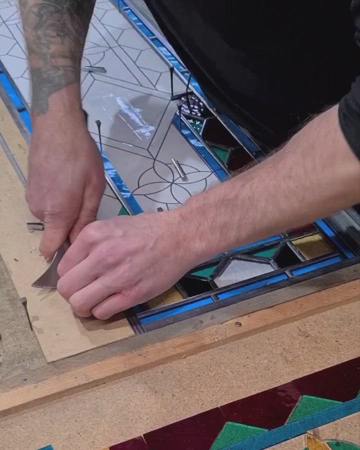 This may contain: a person is working on a stained glass window with scissors and other items in the background