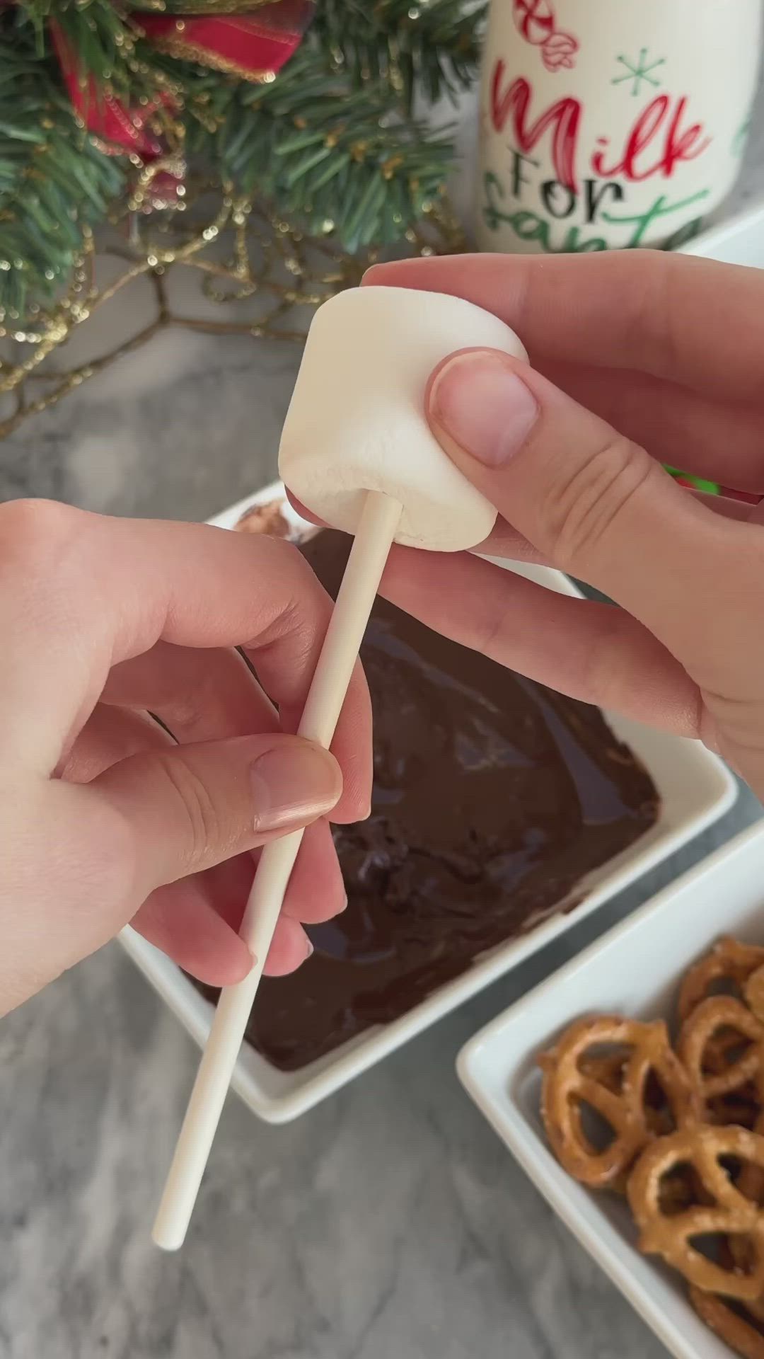 This may contain: a person is holding a chocolate reindeer lollipop with pretzels in the background