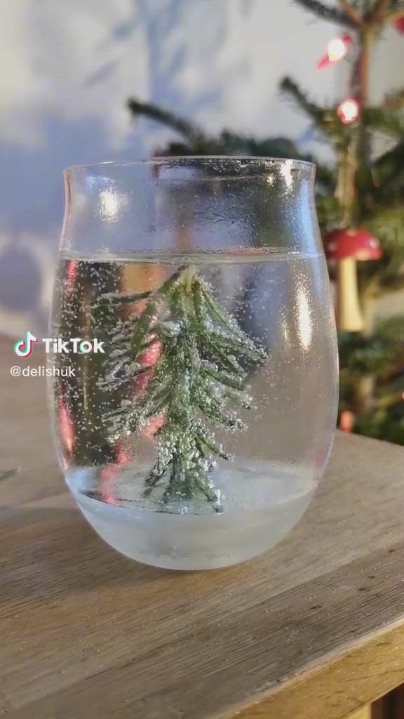 This may contain: a glass filled with water sitting on top of a table next to a christmas tree