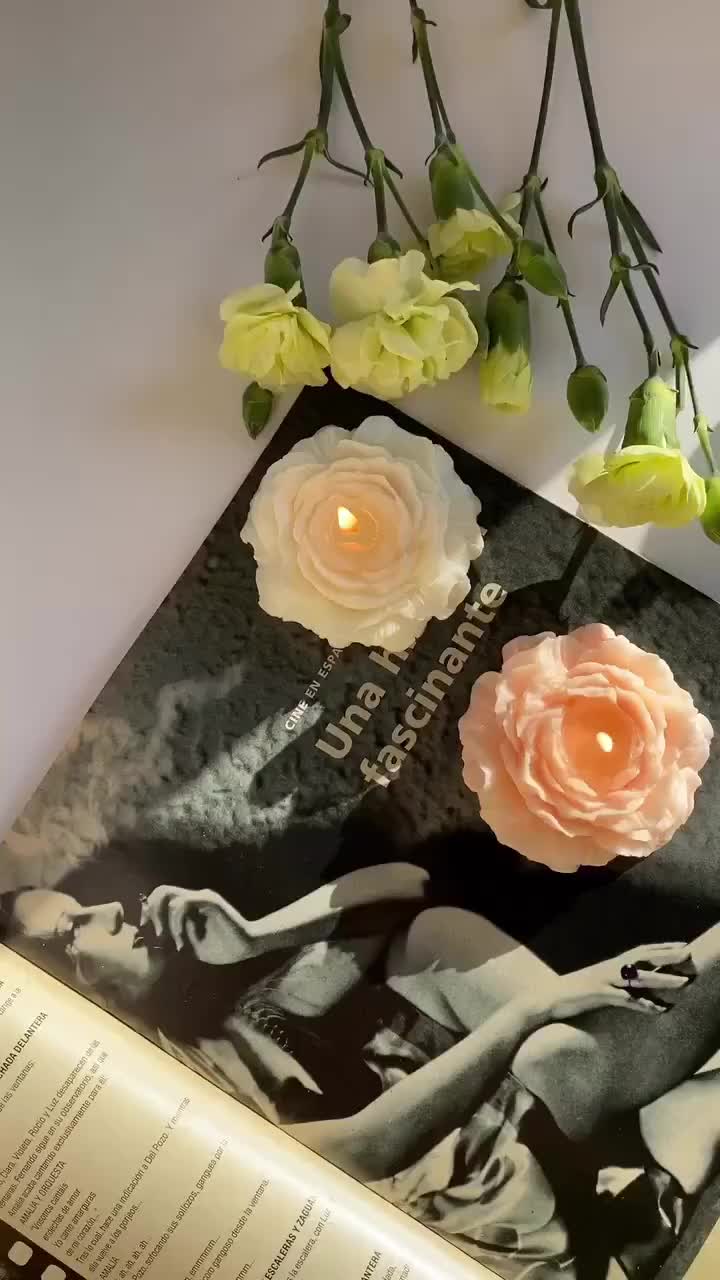 This may contain: an open book with flowers sitting on top of it next to a candle and some books