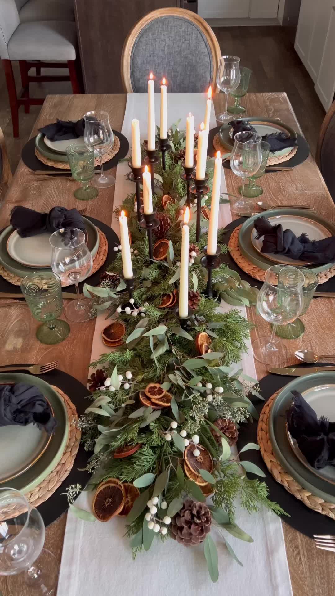 This may contain: a dining room table set for christmas with candles and greenery on the centerpiece