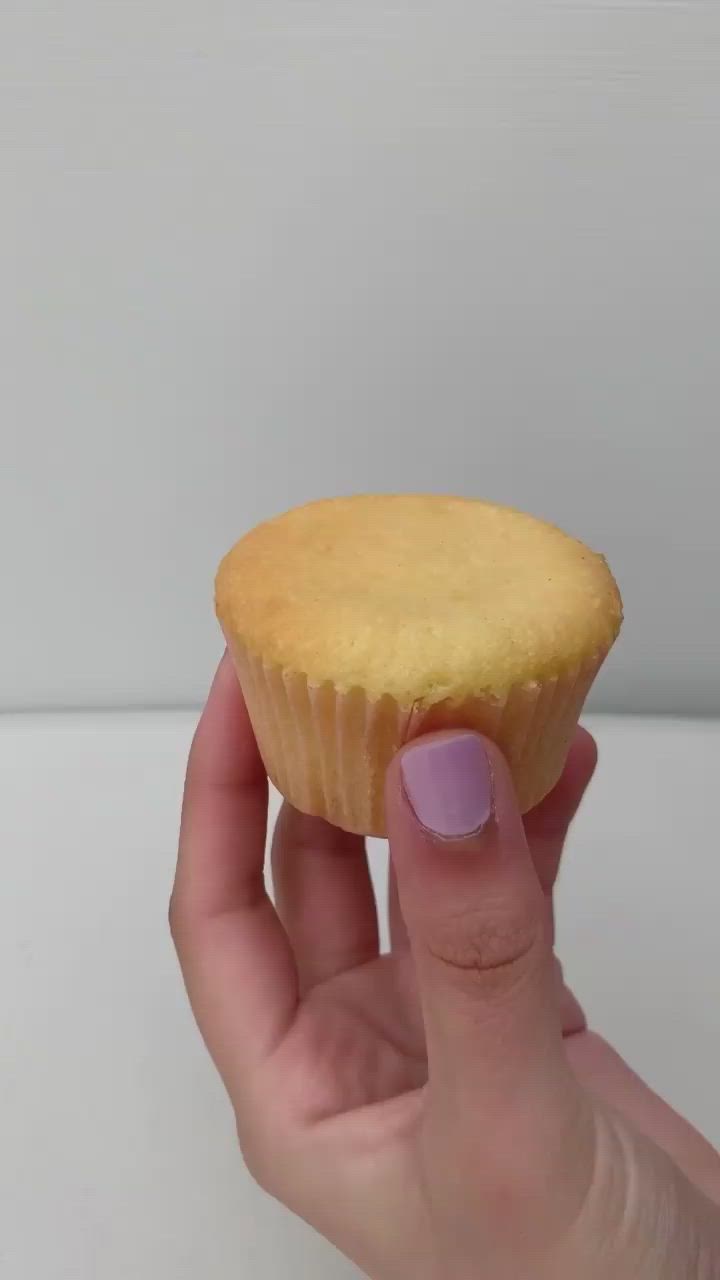 This may contain: a hand holding a cupcake with white frosting and green sprinkles