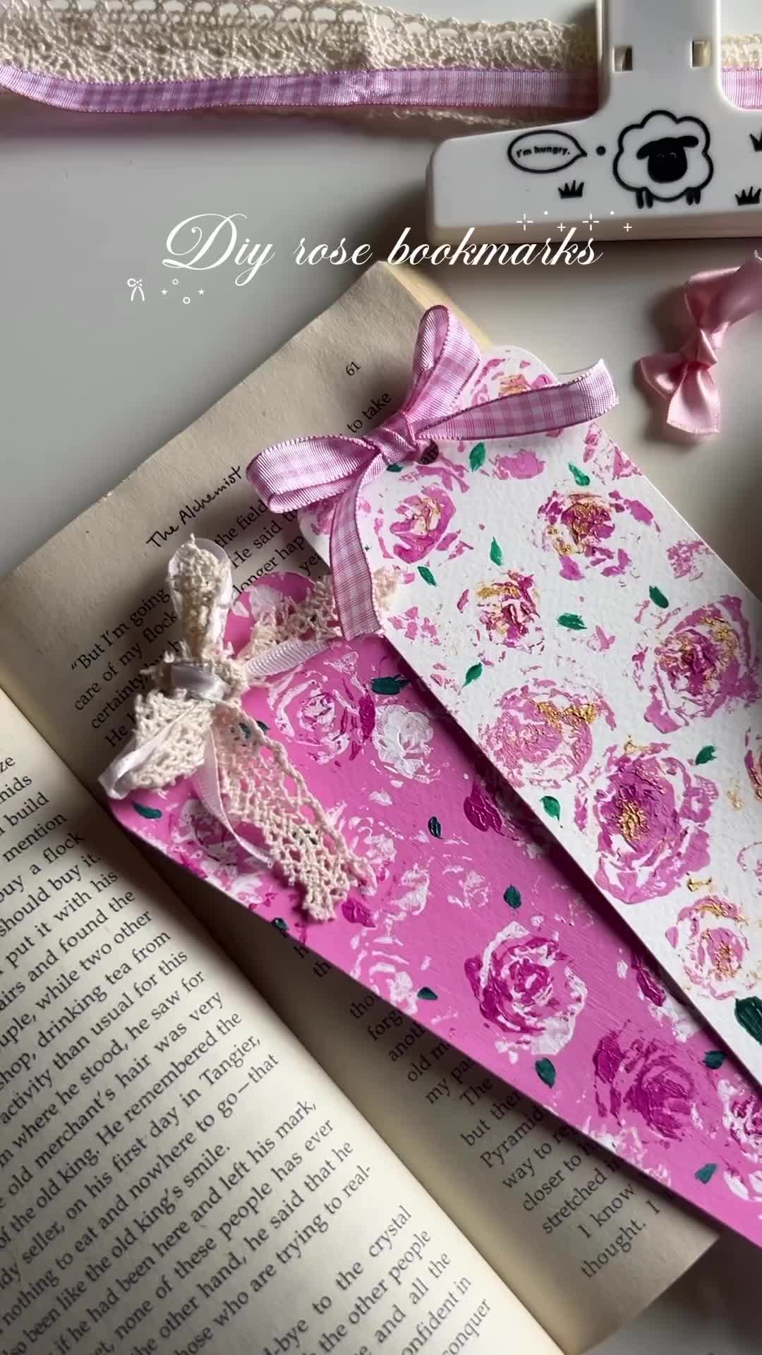 This may contain: an open book with pink flowers on it next to some other books and papers that are laying down