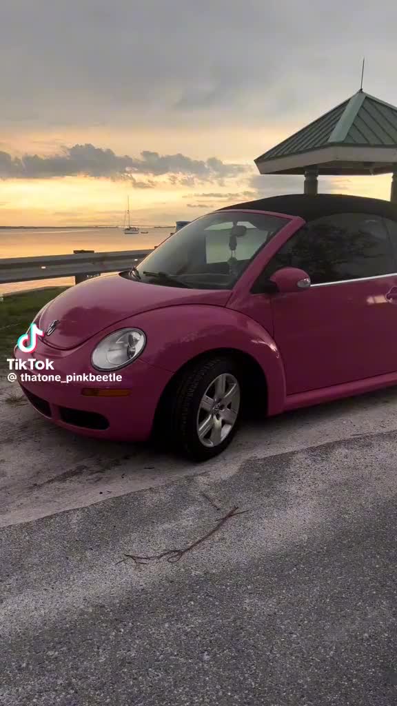 This may contain: a pink convertible car parked in front of a gazebo on the beach at sunset