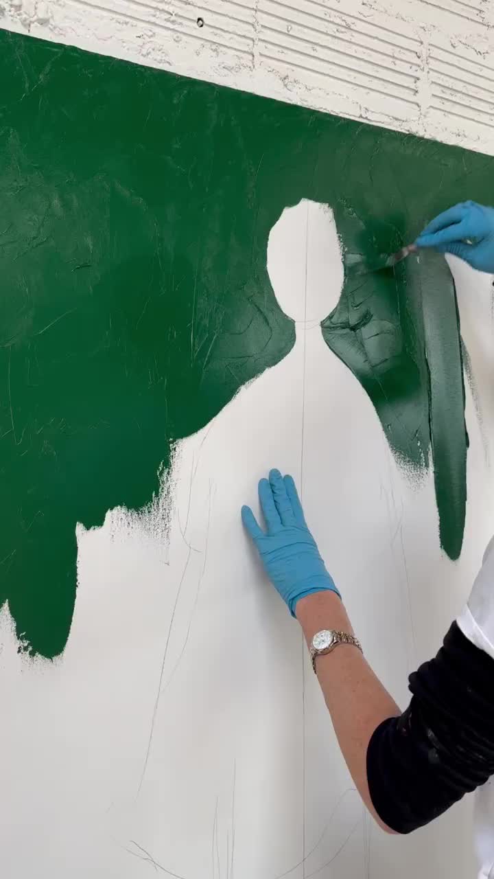 This may contain: a person in blue gloves painting a wall with green and white paint on the walls