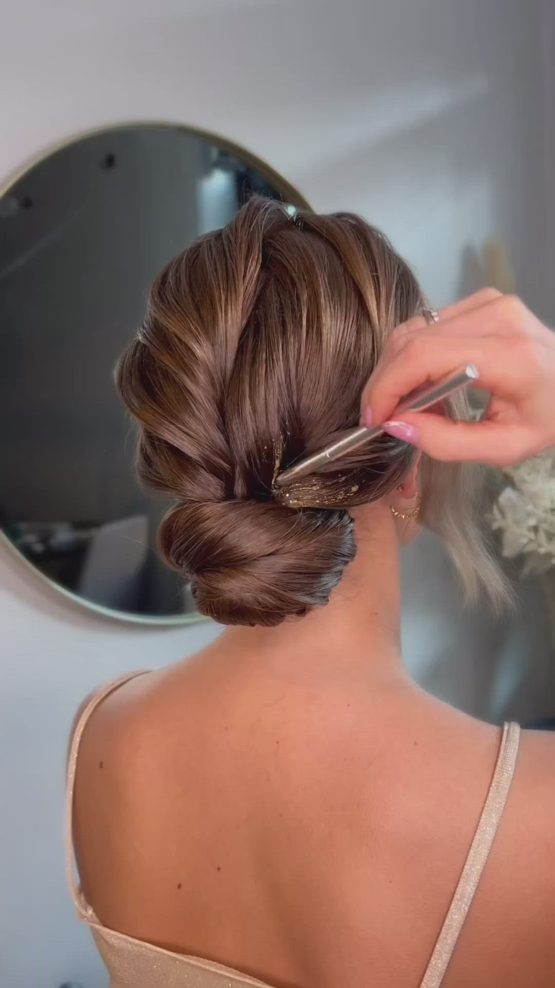 This may contain: a woman with her back to the camera, wearing a gold dress and hair in a low bun