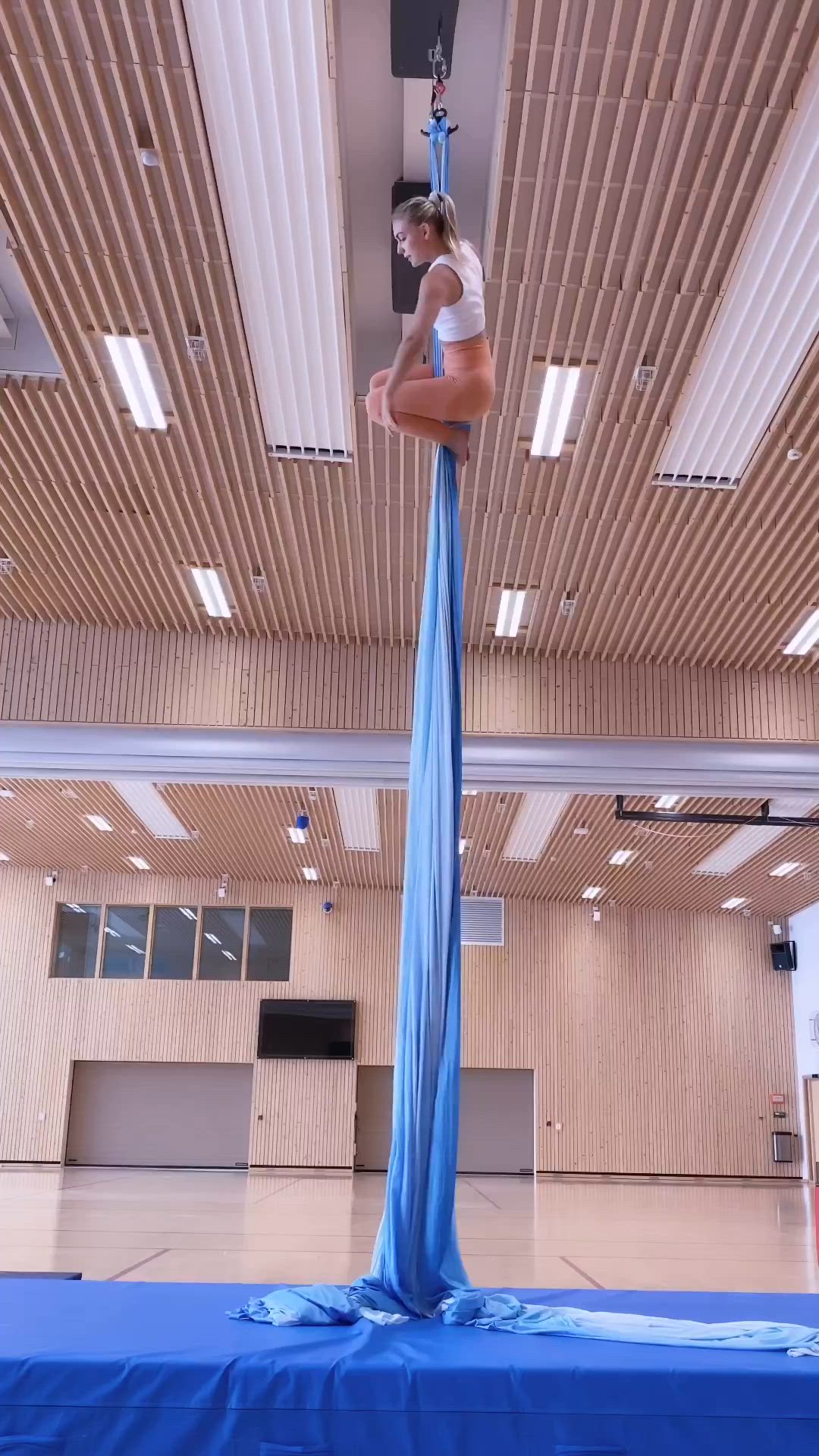 This may contain: a woman is doing aerial acrobatic tricks on a blue mat in an indoor gym