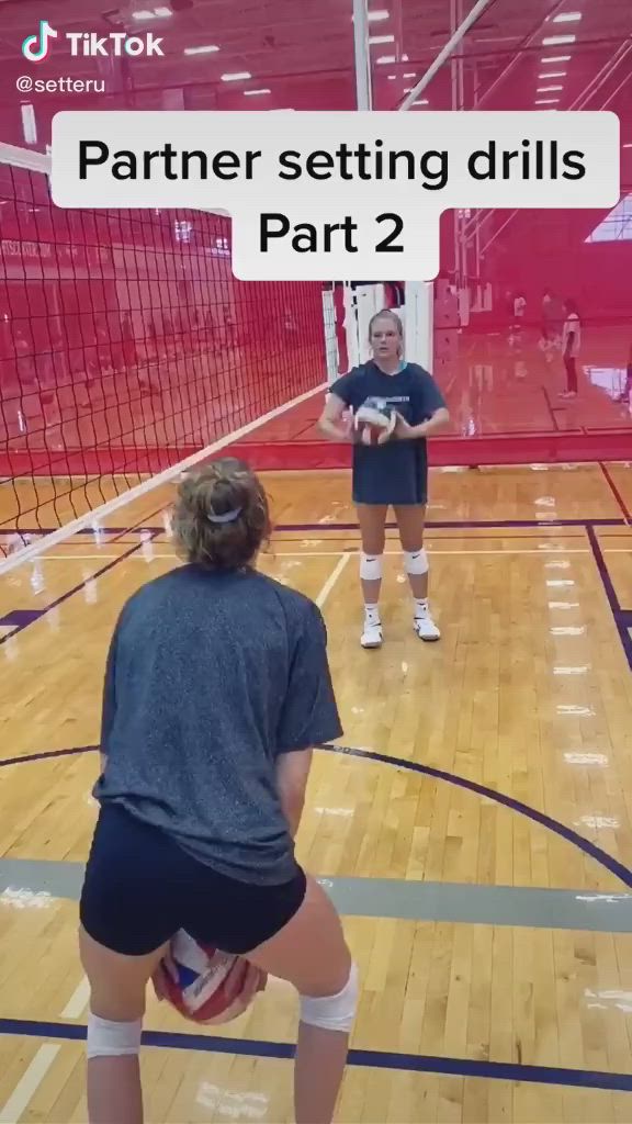 This may contain: two girls are playing volleyball in an indoor gym with one reaching up to hit the ball