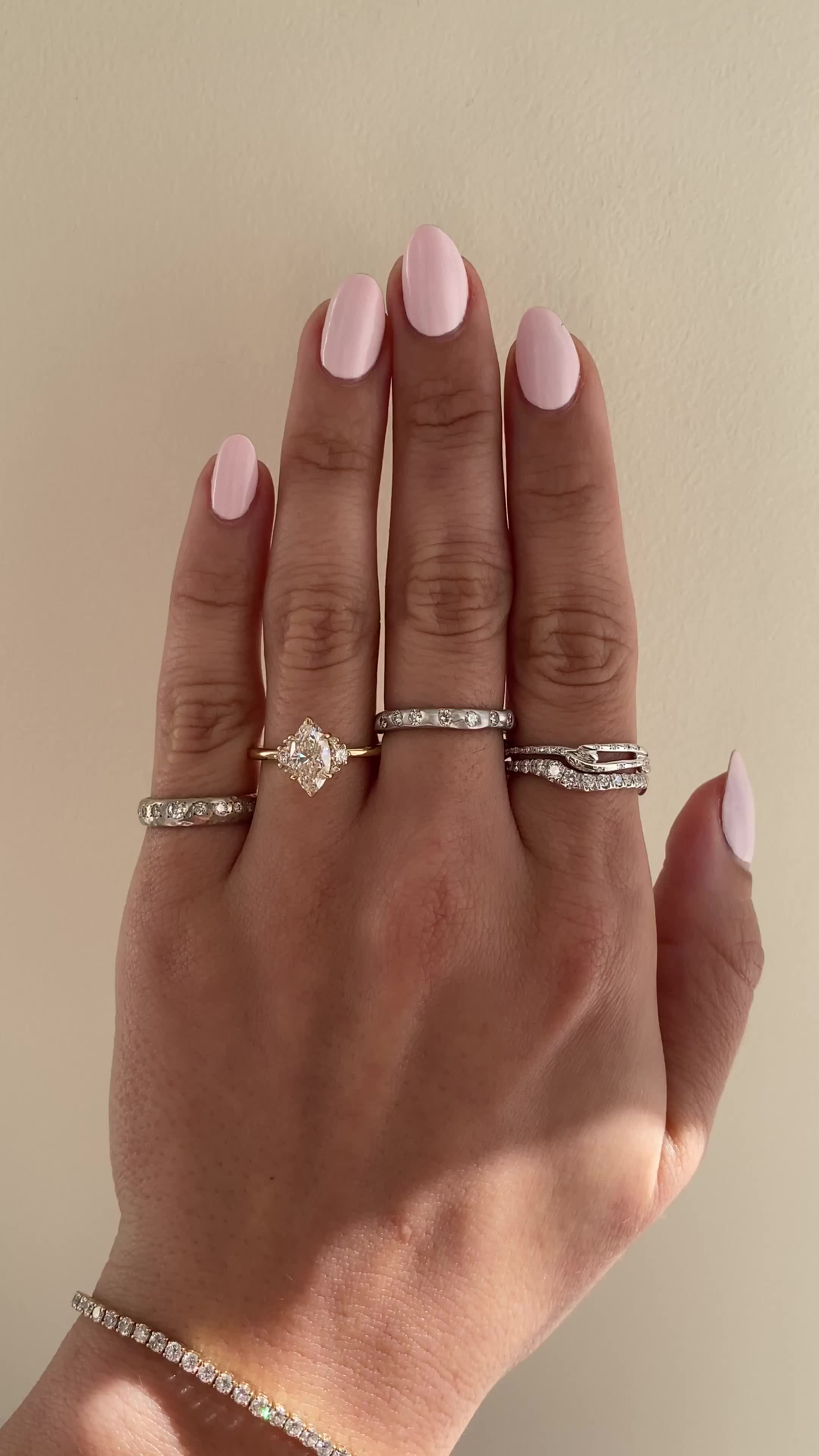 This may contain: a woman's hand with pink manicured nails and three different rings on it