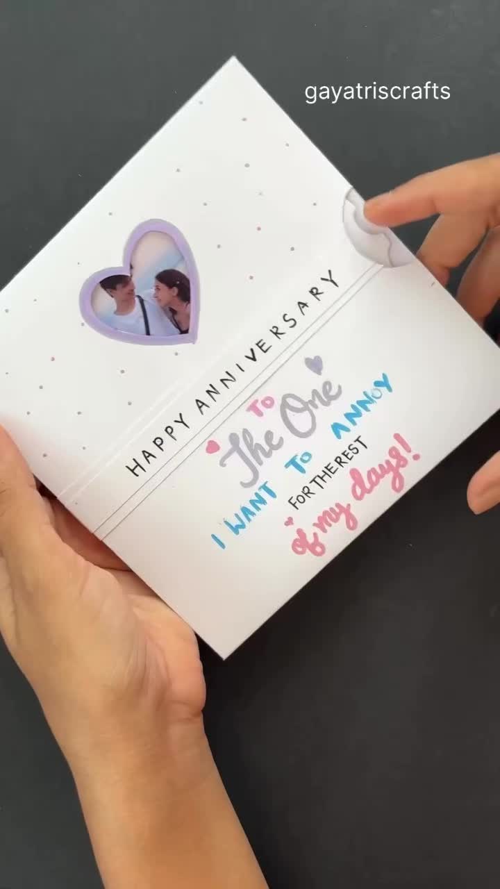 This may contain: two hands holding an anniversary card with the words happy anniversary written on it and hearts