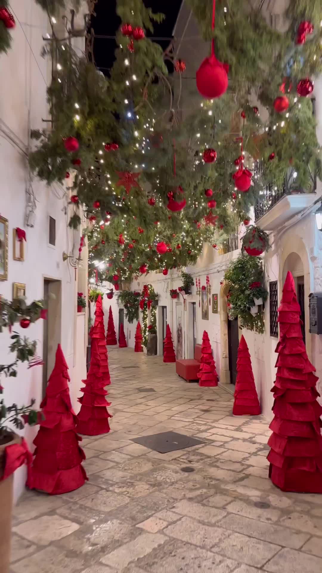 This may contain: red christmas trees are lined up in the middle of an alley with lights strung from them