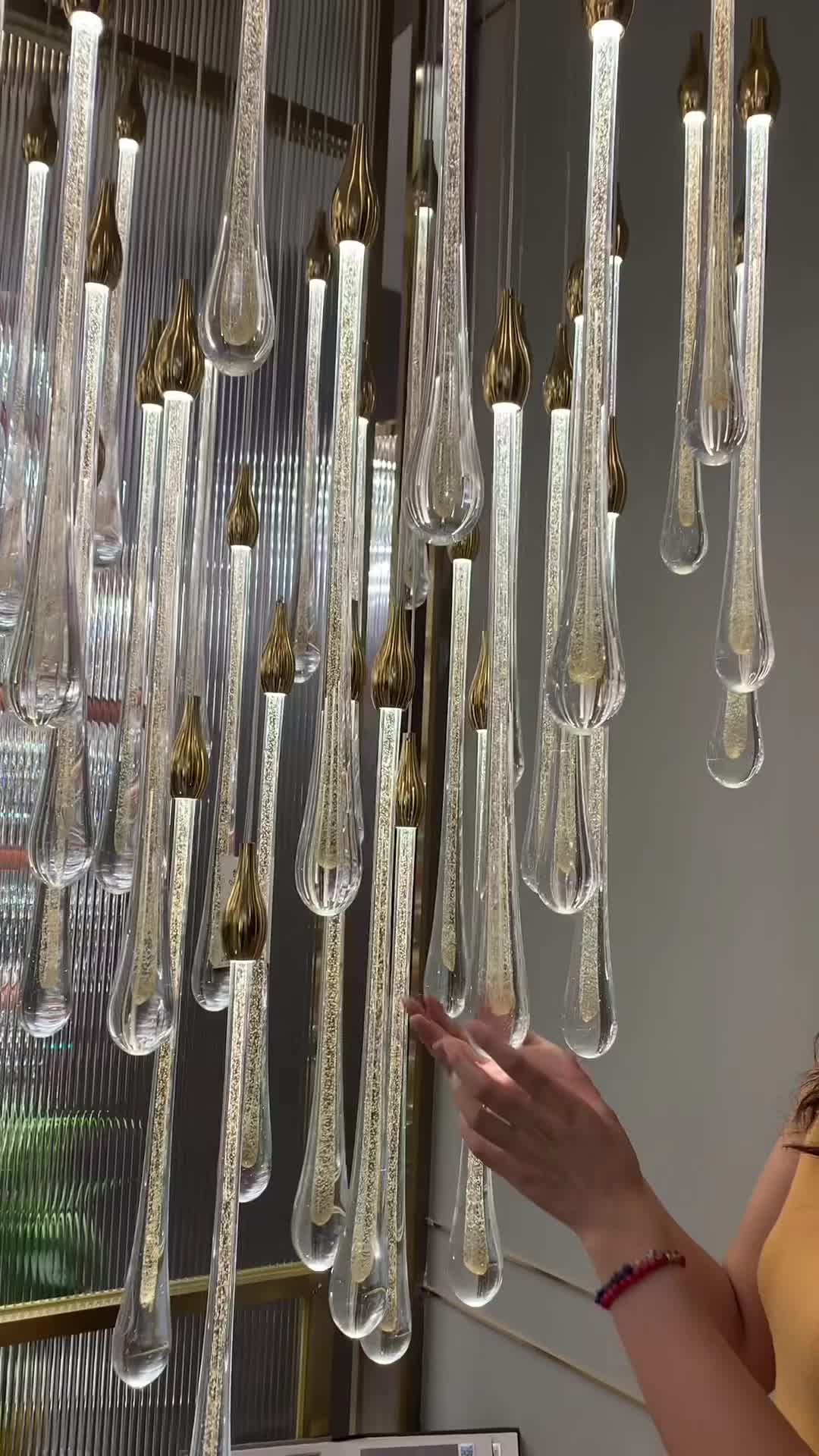 This may contain: a woman standing in front of a chandelier made out of glass bottles and hanging from the ceiling