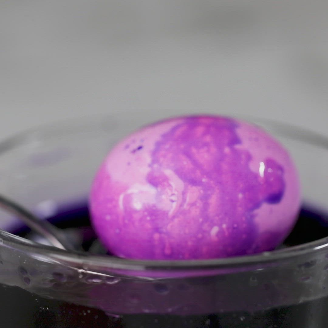 This may contain: a purple substance sitting on top of a spoon in a bowl with liquid inside it