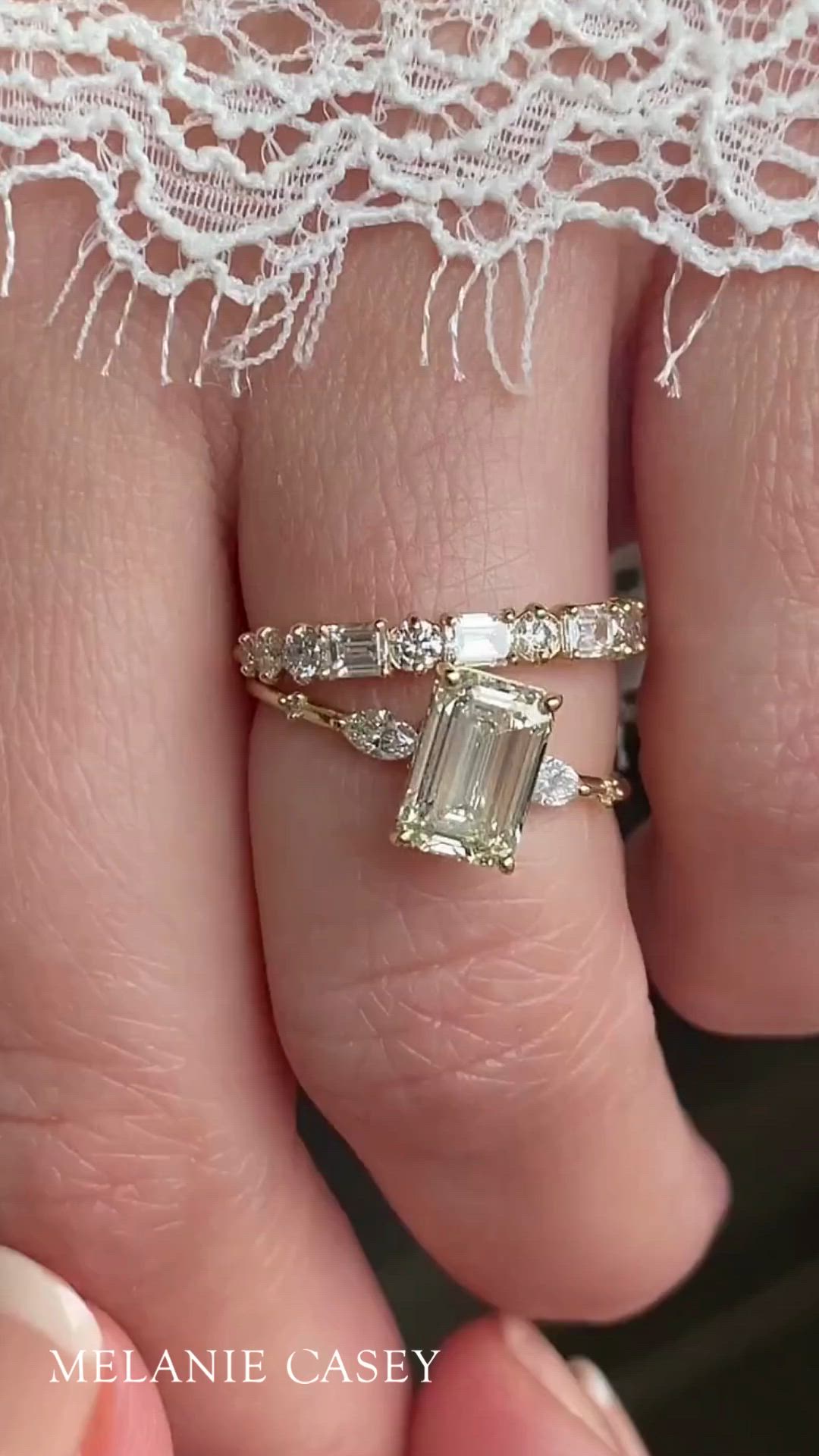 This contains: A woman's hand wearing an emerald cut diamond engagement ring and wedding band.