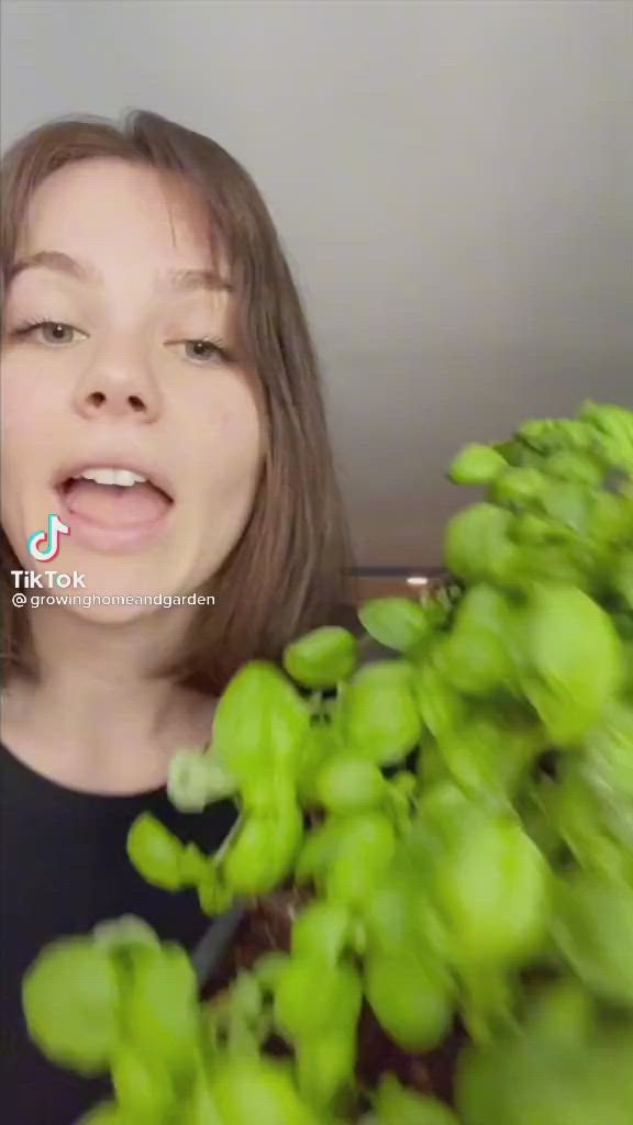 This may contain: a woman is making a funny face as she looks at some green plants in front of her