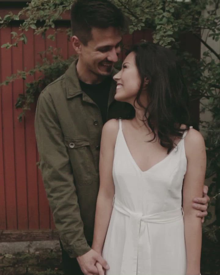 This may contain: a man and woman standing next to each other in front of a red wall with ivy growing on it