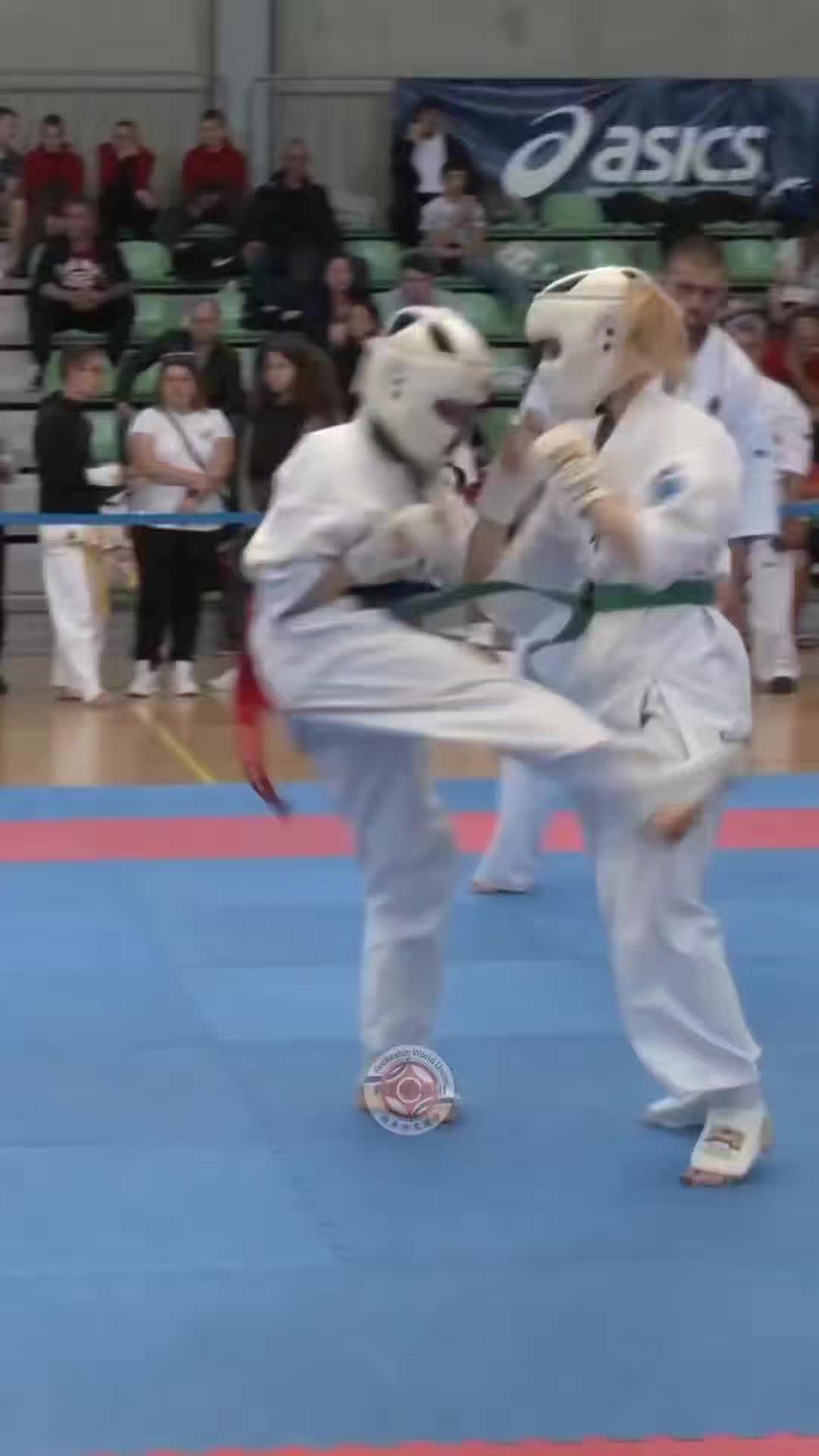 This may contain: two people in white uniforms doing karate on a blue court with an audience behind them