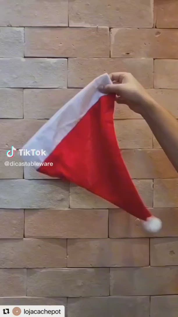 This may contain: a hand holding a red and white christmas hat on top of a brick wall with the word tiktok above it