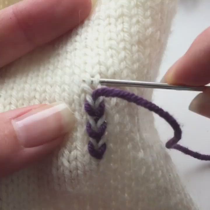 This may contain: someone is stitching the end of a knitted sweater with purple and white yarn