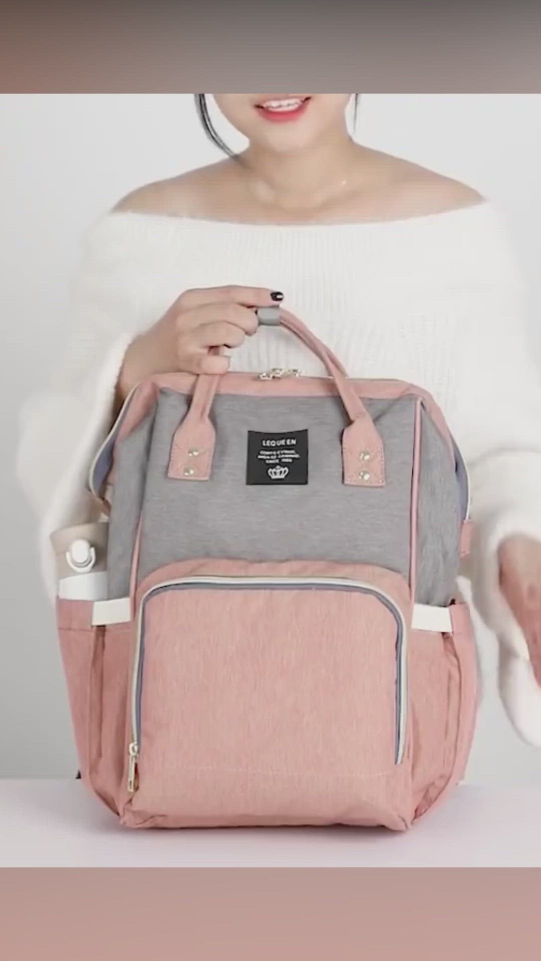 This may contain: a woman holding a pink and grey backpack