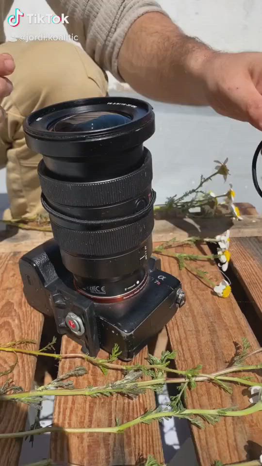 This may contain: a person is holding a camera lens in front of the camera on top of a wooden table