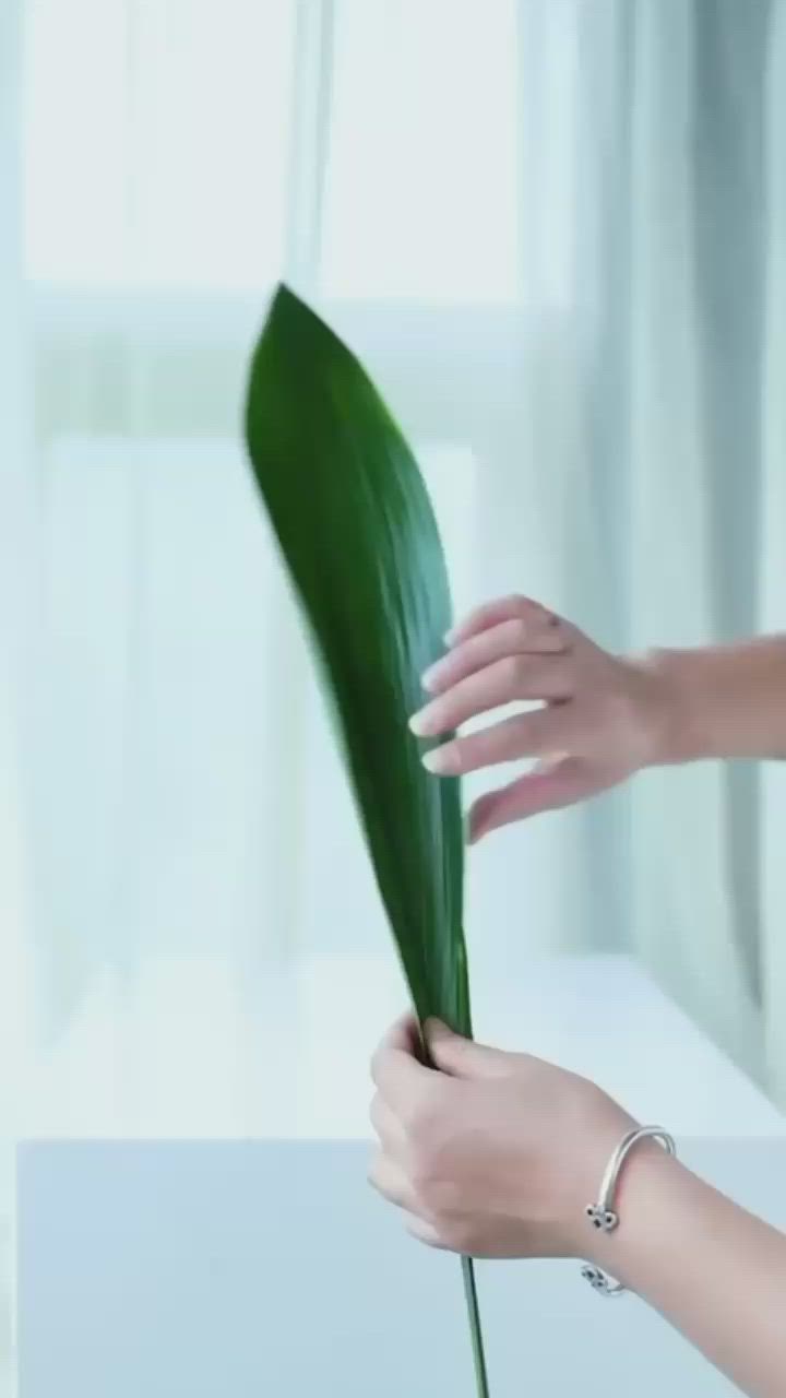 This may contain: a woman is holding a green plant in her hand while sitting at a white table