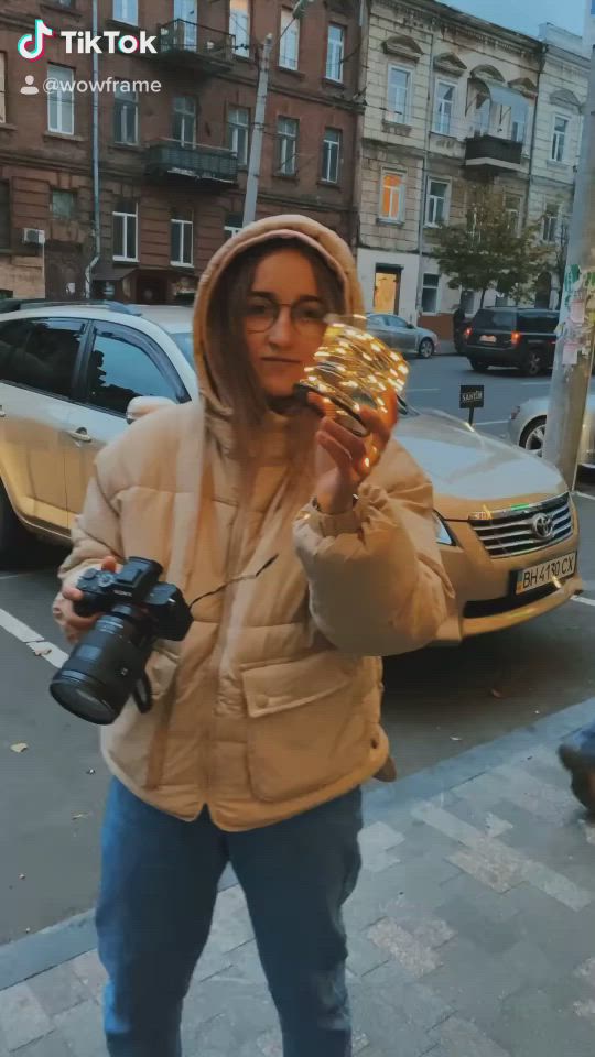 This may contain: a person standing on the sidewalk with a camera and some kind of object in their hand