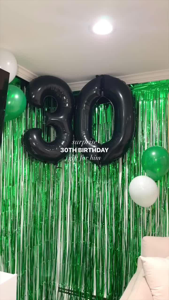 This may contain: a party room with balloons and streamers on the wall, green curtained backdrop