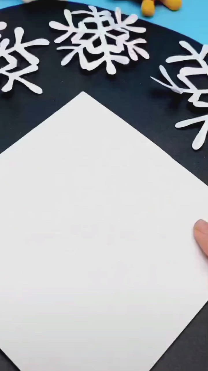 This may contain: someone is making snowflakes out of paper on a black surface with white snow flakes