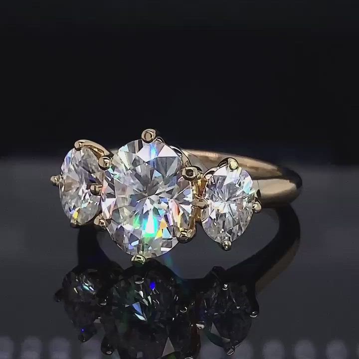 This may contain: three stone diamond ring with reflection on black surface