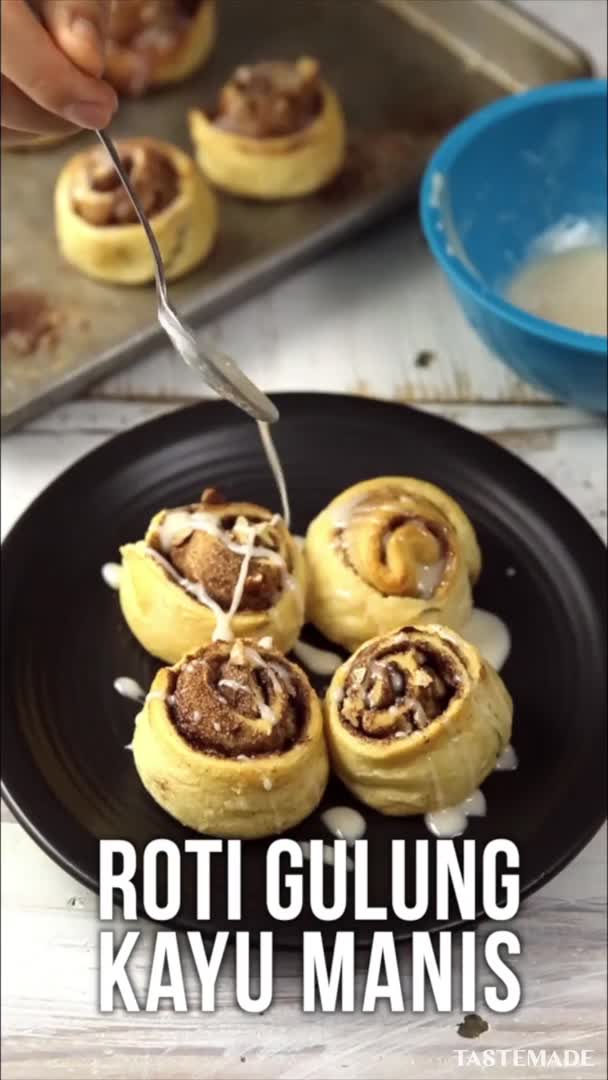 This may contain: several cinnamon rolls on a black plate next to a baking pan and blue dish towel