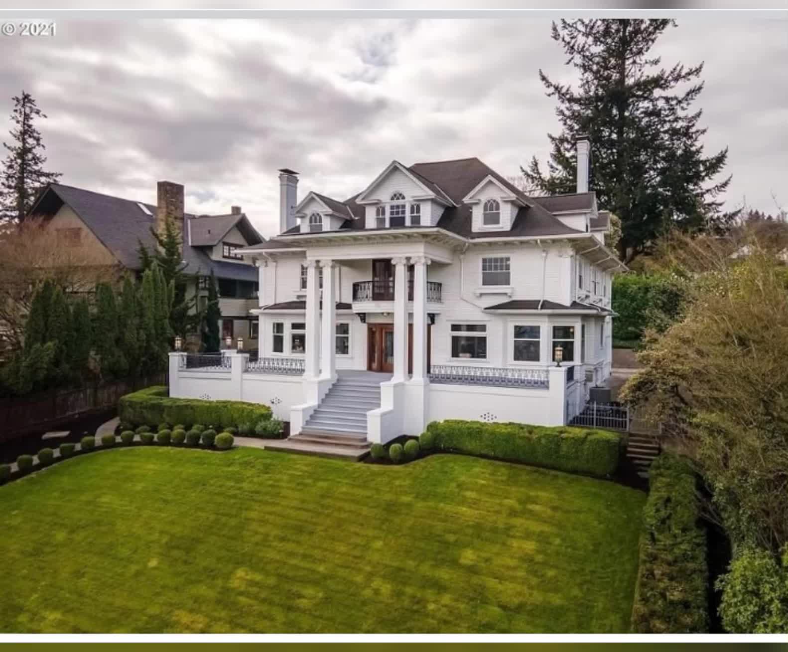 This may contain: an aerial view of a large white house in the middle of a green yard with trees and bushes