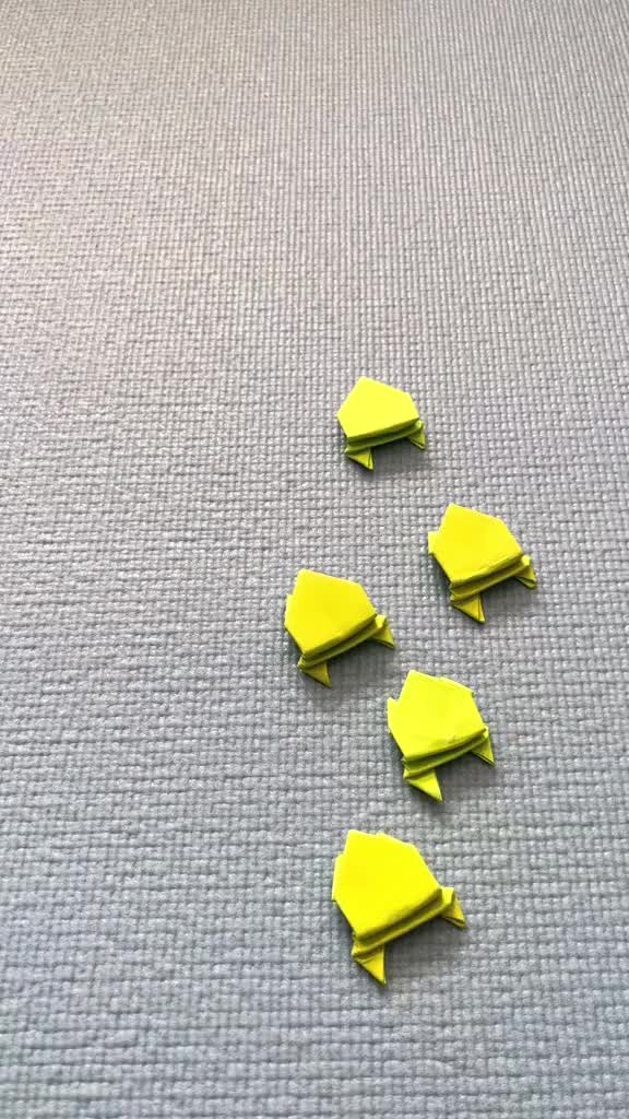 This may contain: a hand is pointing at four small yellow origami turtles on the floor,